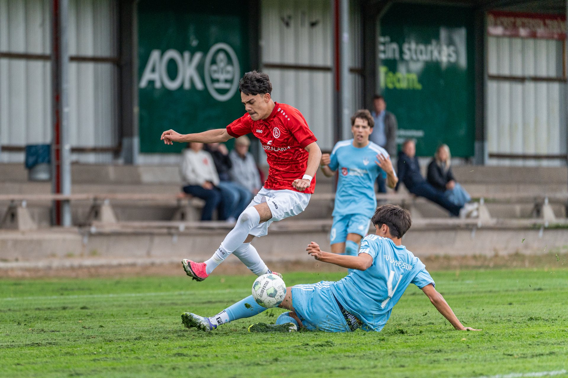 Spieler von ATS Buntentor überspringt einen grätschenden Spieler von JFV Weyhe-Stuhr im Zweikampf um den Ball