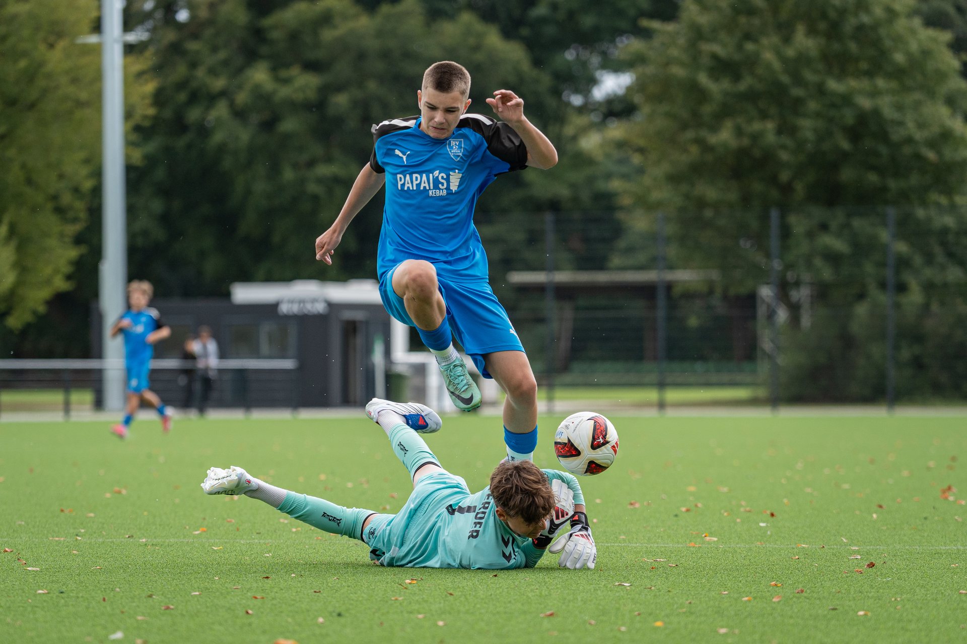 Spieler von JFV Weyhe-Stuhr springt über einen am Boden liegenden Torhüter, während der Ball daneben liegt