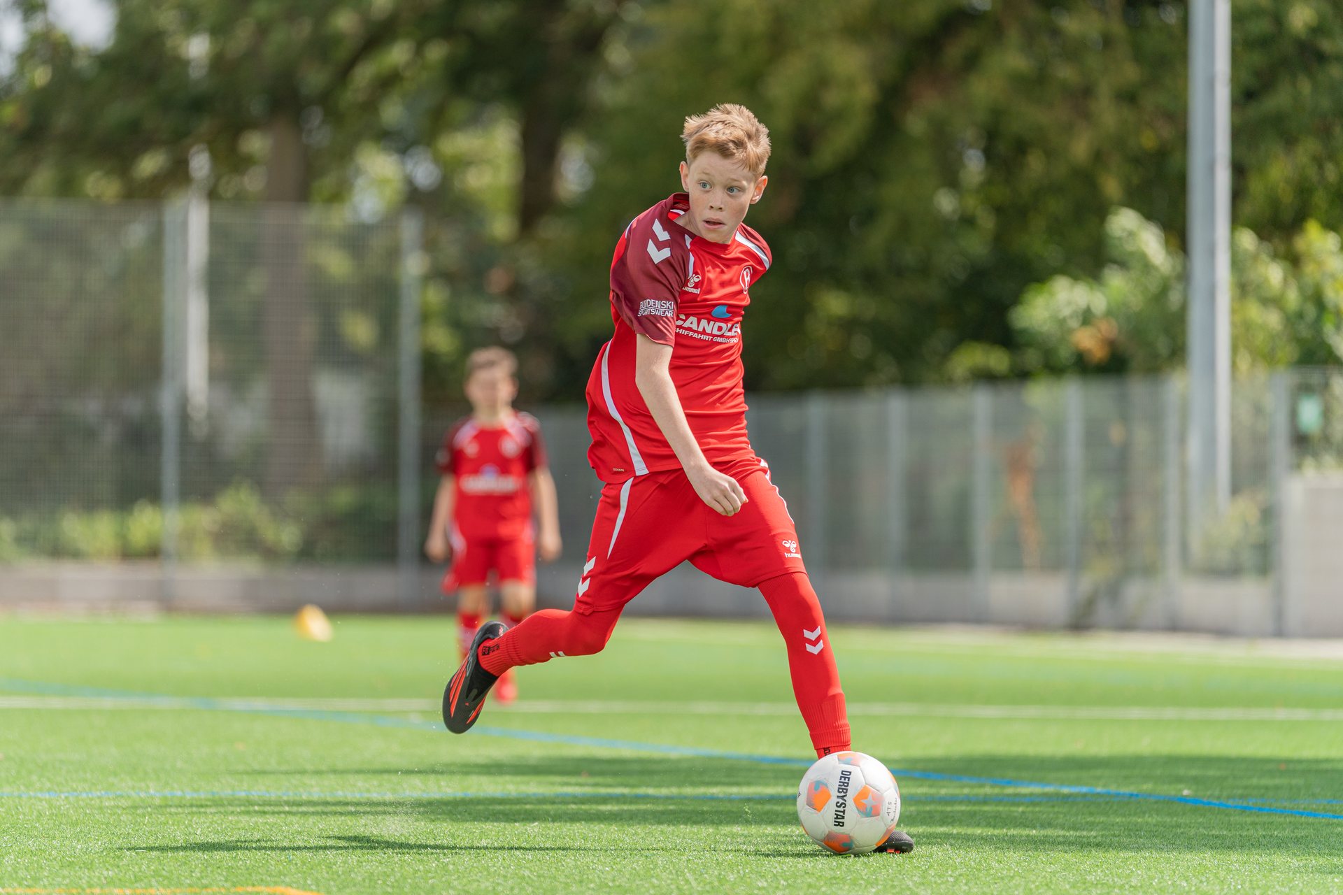 Junger Fußballspieler im roten Trikot am Ball