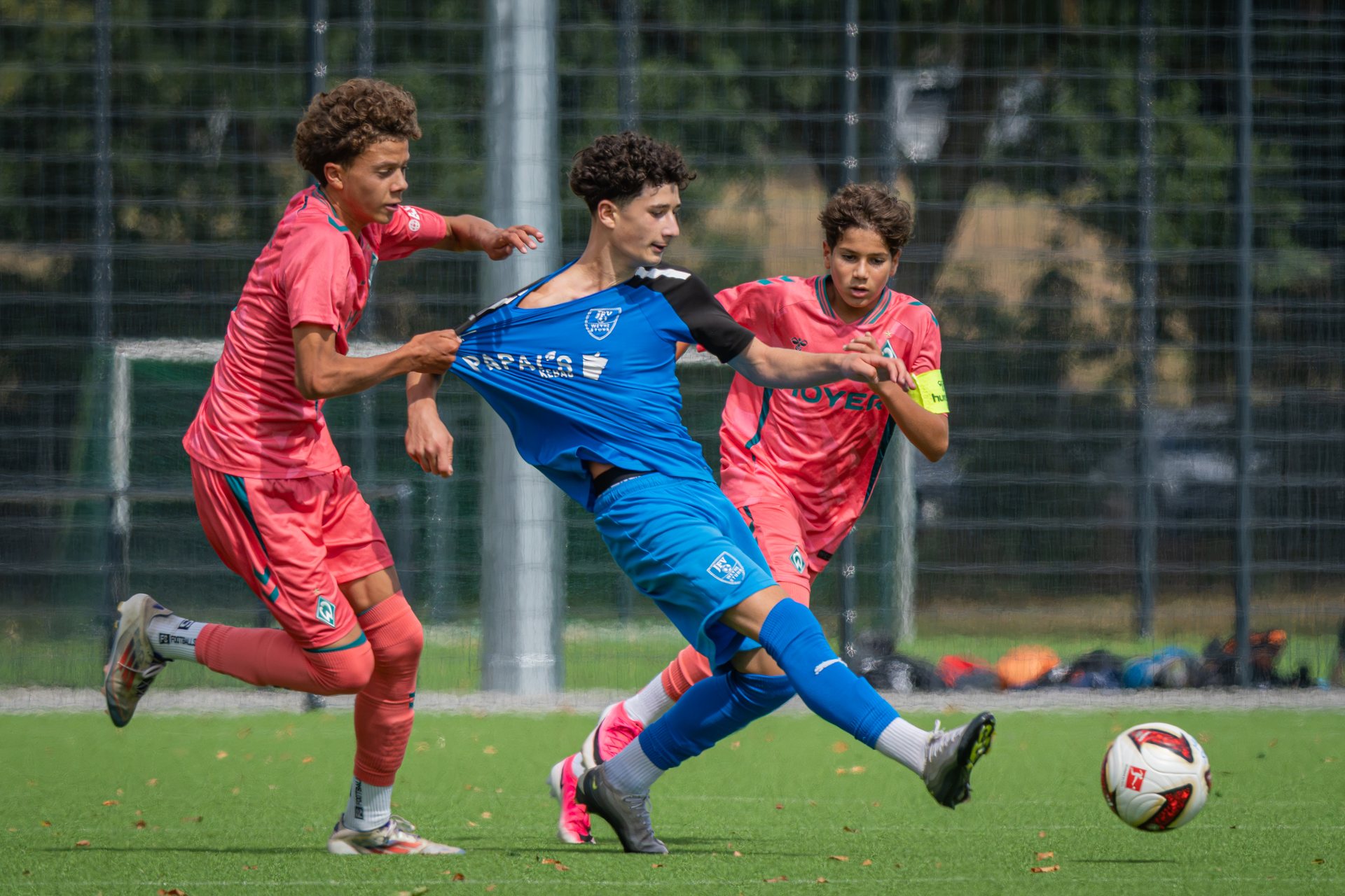 Zwei Spieler von SV Werder Bremen und ein Spieler von JFV Weyhe-Stuhr laufen zum Ball