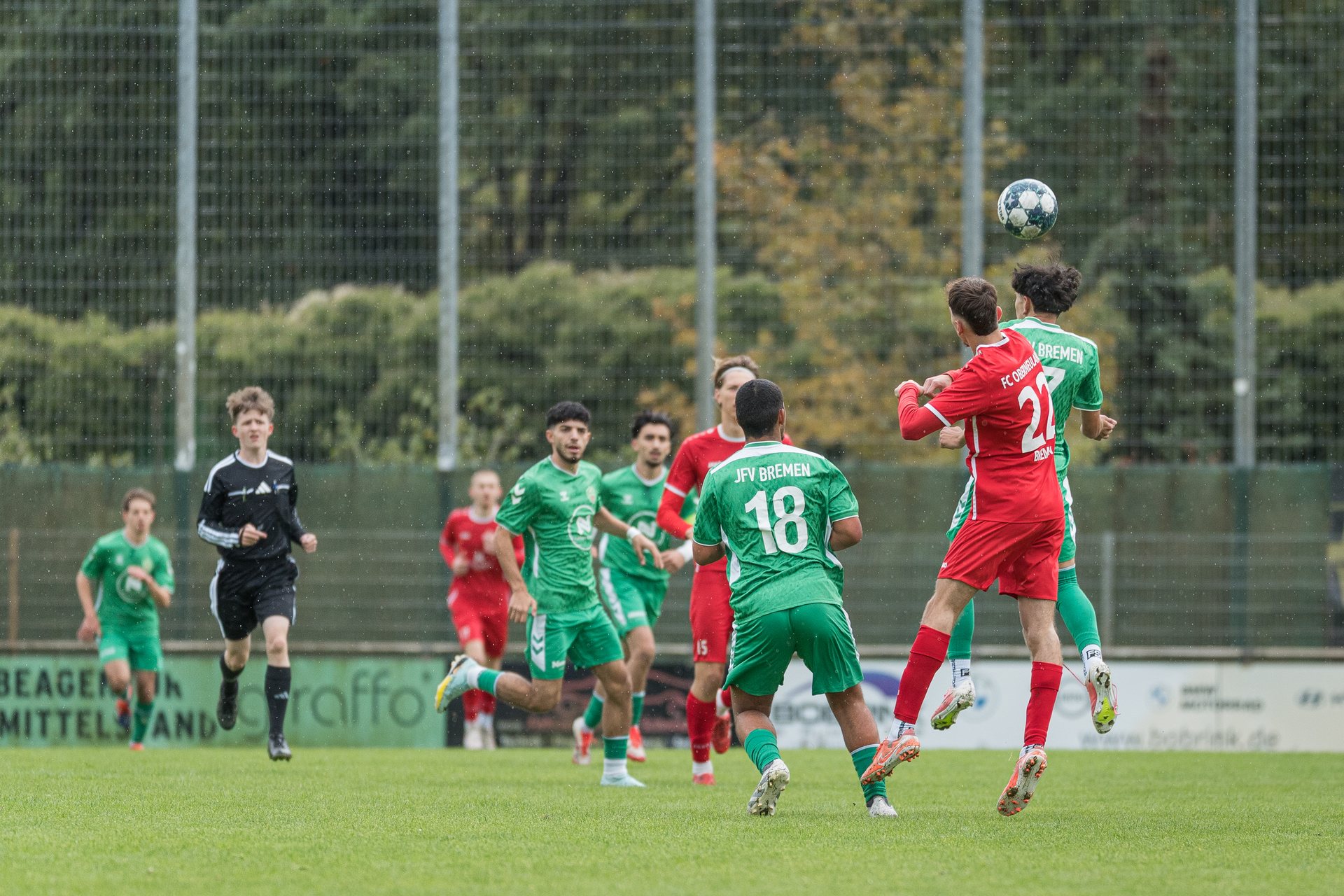 Spieler von FC Oberneuland und JFV Bremen II springen im Regen zum Kopfball