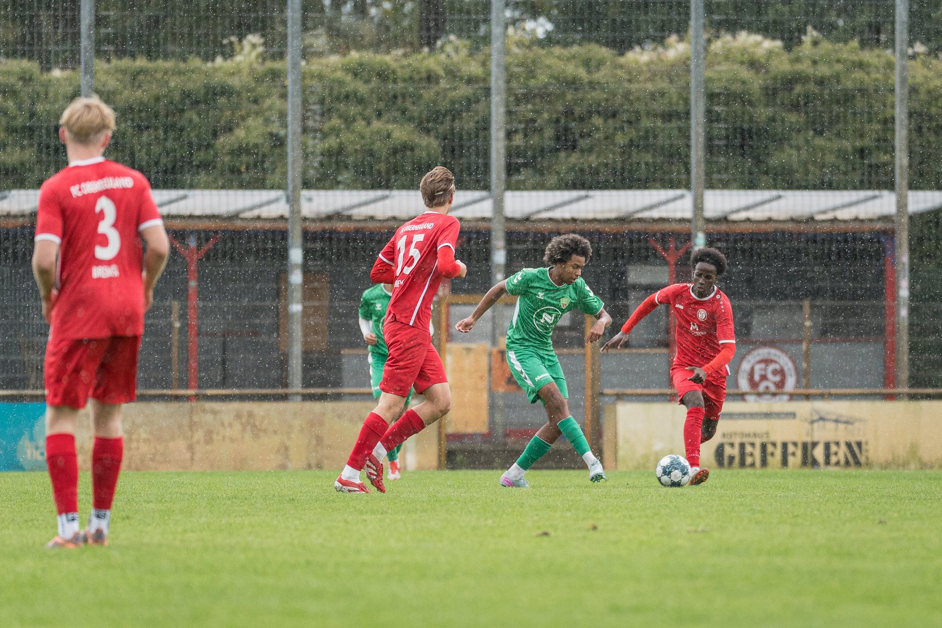 Spieler von FC Oberneuland und JFV Bremen II gehen im Regen mit ausgestrecktem Fuß zum Ball